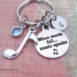 May include: Silver keychain with a music note charm, a blue crystal charm, a round charm with the letter "S" engraved on it, and a round charm with the text "When words fail... music speaks" engraved on it.