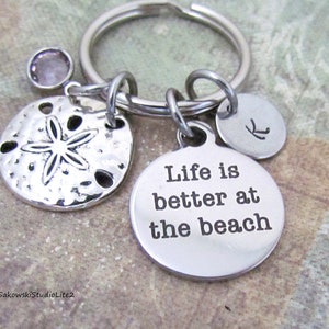 May include: Silver keychain with a charm that says "Life is better at the beach", a sand dollar charm, a small pink crystal charm, and a charm with the letter "K" engraved on it.