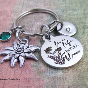May include: Silver keychain with a green crystal charm, a silver edelweiss charm, and a round silver charm with the engraved text "Live life in full bloom".