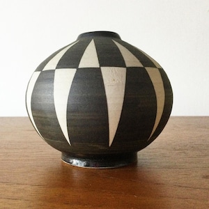 May include: A spherical ceramic vase featuring a matte black finish with a repeating pattern of cream-coloured vertical triangles. The vase has a narrow circular opening at the top and sits on a small, slightly raised circular base.