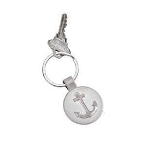 May include: Silver key chain with a round anchor charm. The key chain has a silver ring and a silver key attached to it.