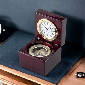 Könnte beinhalten: Eine Uhr aus Mahagoniholz mit einem Kompass im Inneren. Das Zifferblatt der Uhr hat römische Ziffern und goldene Zeiger. Der Kompass hat eine goldene Nadel und ein weißes Zifferblatt mit schwarzen Markierungen.