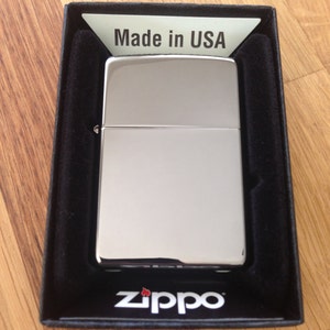 May include: A silver Zippo lighter in a black box with the words "Made in USA" and "Zippo" printed on it.