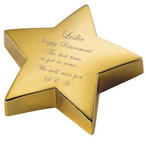 May include: A gold star-shaped paperweight with an engraved message that reads "Leslie Happy Retirement The best time is yet to come... We will miss you SCH".