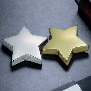 May include: Two stars, one silver and one gold, are displayed on a black surface. The stars are three-dimensional and have a shiny finish.