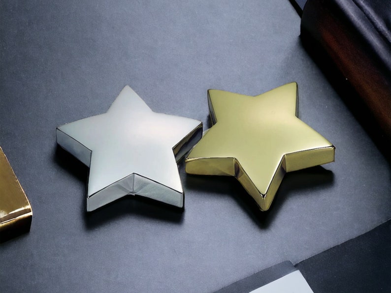 May include: Two stars, one silver and one gold, are displayed on a black surface. The stars are three-dimensional and have a shiny finish.