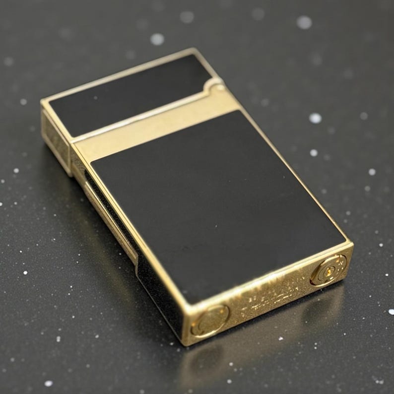 May include: A rectangular lighter with a gold-colored frame and black panels. The lighter has a classic design with a hinged lid and a textured surface. The lighter is a stylish accessory.