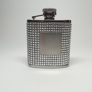 Pode incluir: Uma garrafa de prata com um padrão de diamante na frente. A garrafa tem uma tampa de prata e uma superfície lisa e plana no centro.