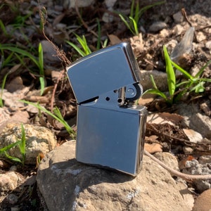 May include: A silver lighter with a textured finish. The lighter is closed and sitting on a rock.