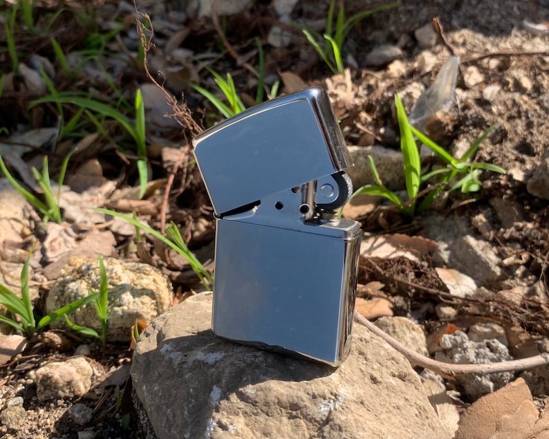 May include: A silver lighter with a textured finish. The lighter is closed and sitting on a rock.