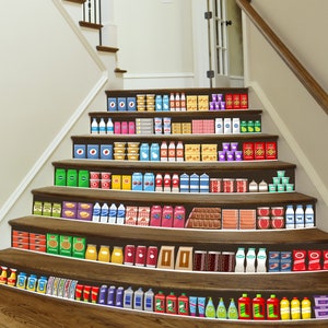 Op de afbeelding: Trap versierd met stickers die lijken op supermarkt schappen. De stickers tonen diverse voedingsmiddelen, waaronder melkpakken, conserven en verpakte voedingsmiddelen. De trap is van hout, met een witte muur aan de zijkant.