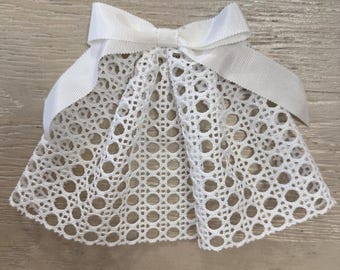 Puede incluir: Lazo para el pelo de encaje blanco con una cinta de satén blanca atada en un lazo. El encaje es un diseño delicado y calado con pequeños círculos.