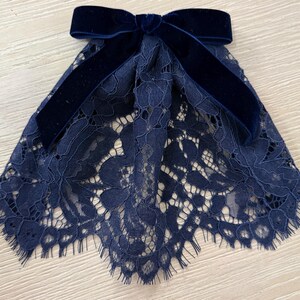 Può includere: Un colletto in pizzo blu navy con un fiocco di velluto. Il pizzo è finemente lavorato e il fiocco di velluto è centrato nella parte superiore. Il colletto è progettato per essere indossato intorno al collo.