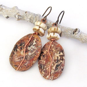 May include: A pair of earrings with brown and white stone beads and copper wire accents. The stones are oval shaped and have a mottled brown and white pattern.
