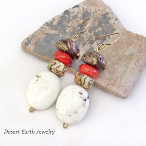 May include: White, red, and brown beaded dangle earrings with gold hooks. The earrings feature a large white oval bead, a smaller white bead, a red bead, and two brown seed beads.