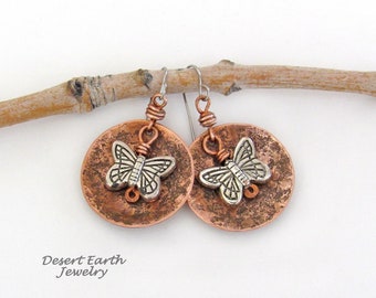 May include: Copper and silver butterfly earrings with a hammered texture. The earrings are hanging from a branch.