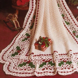 May include: A white crocheted blanket with a red and green holly border. The blanket is draped over a red surface and a small gift box is in the foreground.