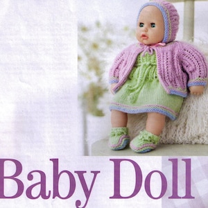 Op de afbeelding: Een gebreide babypop-outfit in roze en groen. De outfit bestaat uit een vest, een jurk en slofjes. De pop zit op een wit, pluche oppervlak. De tekst "Baby Doll" is onder de afbeelding gedrukt.