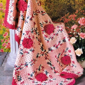 May include: A pink and red crocheted throw blanket with a floral design. The blanket is draped over a white column and has a red border.