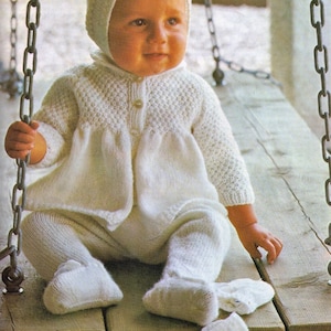 Puede incluir: Un conjunto de bebé de punto blanco con un gorro a juego. El conjunto incluye un cárdigan con cierre de botón y pantalones con botines.