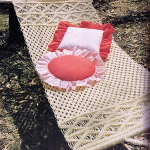 May include: A white macrame hammock with a red and white pillow and a pink and red pillow. The hammock is hanging from a tree branch.