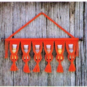 May include: A red macrame wall hanging with six small glass jars hanging from it. The jars are clear and have a white lid. The wall hanging is made with a knot pattern and has tassels on the bottom.