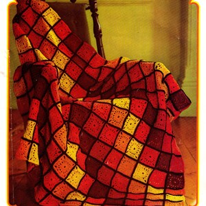 Peut inclure: Une couverture en crochet dans les tons rouge, orange et jaune. La couverture est faite de carrés avec un motif géométrique et est drapé sur une chaise en bois.