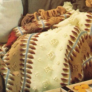 May include: A crocheted throw blanket with a white background and brown, red, and blue stripes. The blanket has a textured pattern and is folded on a sofa.