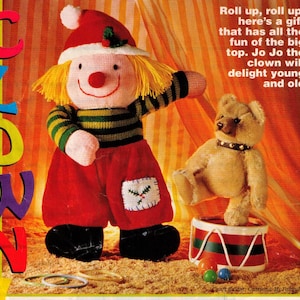 May include: A knitted clown doll wearing a red and white Santa hat, red pants, and a green and yellow striped shirt. The doll is holding a red and green drum with a teddy bear sitting on top. The text "Roll up, roll up, here's a gift that has all the fun of the big top. Jo Jo the clown will delight young and old" is printed on the background.