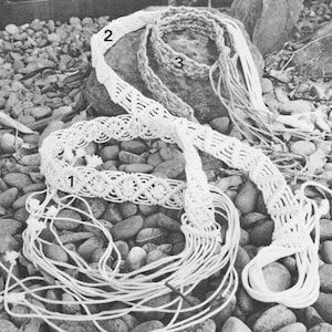 May include: Three macrame belts made with white cord. The belts are laid out on a bed of small gray rocks. The belts are numbered 1, 2, and 3.