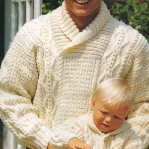 May include: A white cable knit sweater with a wide collar. The sweater is worn by a person holding a child wearing a similar sweater.
