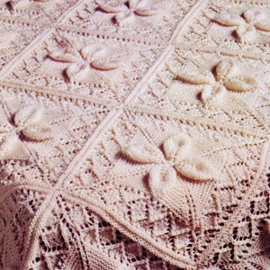 Pode incluir: Um close-up de um cobertor de crochê com um delicado padrão floral em uma cor rosa claro.