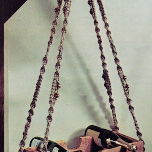 May include: A wooden wine rack with a macrame hanging system. The rack is filled with wine bottles and has a rustic look.