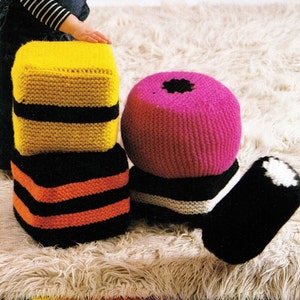 May include: Four knitted ottoman footstools in the shape of licorice candies. The footstools are yellow, black, orange, pink, and white.