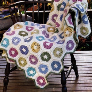May include: A crocheted blanket with a hexagonal pattern in shades of pink, blue, green, and yellow. The blanket is draped over a wooden chair.