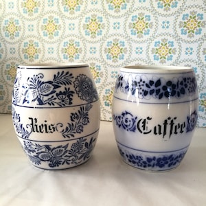 Può includere: Due barattoli di ceramica bianca con disegni floreali blu e bianchi. I barattoli sono etichettati con "Reis" e "Coffee".