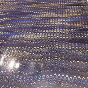 Op de afbeelding: Een close-up van een donkerblauw, wit en geel marmerpapier met een draaiend patroon.