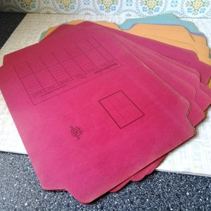 Könnte beinhalten: Ein Stapel roter Aktenordner mit einem karierten Abschnitt und dem Wort "Stundenplan" auf der Vorderseite. Die Ordner haben ein kleines Logo unten rechts.