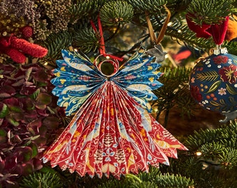 May include: A red and blue paper angel ornament with a folded design, hanging on a Christmas tree.