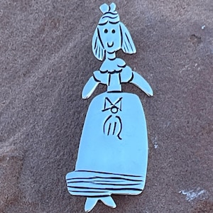 May include: A silver charm shaped like a stick figure of a girl wearing a dress and a crown. The charm is detailed with a bow and a small heart on the dress.