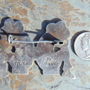 May include: Silver tone pin with two figures holding hands. The back of the pin has the markings "TAVCC" and "920".