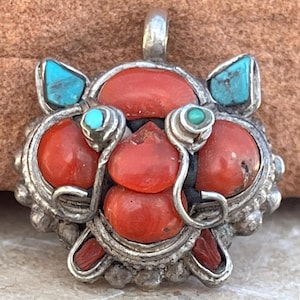 May include: A silver pendant with a red coral and turquoise design. The pendant is made of silver and features a cluster of red coral stones surrounded by turquoise stones. The pendant is a unique and beautiful piece of jewelry.