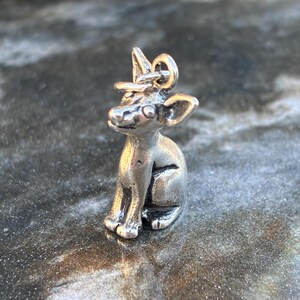 Puede incluir: Un peque&ntilde;o dije plateado con forma de gato sentado con sombrero. El dije tiene detalles, incluyendo orejas grandes y una peque&ntilde;a cola. El gato est&aacute; sentado erguido, con las patas delanteras apoyadas en el pecho. El dije est&aacute; dise&ntilde;ado para ser adjuntado a un collar o pulsera.