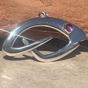 May include: A silver pendant in the shape of a fish with a purple amethyst gemstone set in the eye.