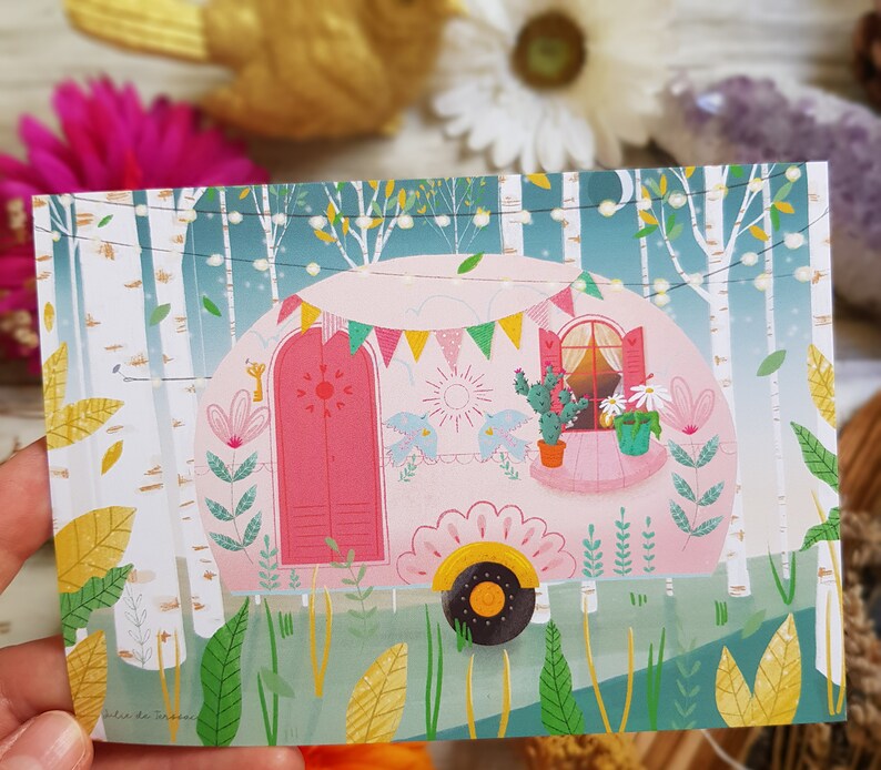 May include: A pink camper van with a white trim and a window with a view of green plants. The camper van is surrounded by green trees and bushes. The camper van has a sign that says 'Alice de Moraes'.
