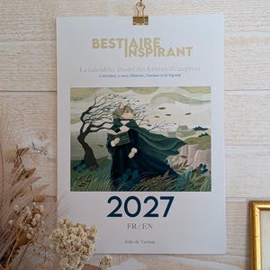 Może przedstawiać: Kalendarz ścienny na 2027 rok zatytułowany BESTIAIRE INSPIRANT z ilustracją postaci w ciemnozielonej pelerynie w wietrznym krajobrazie z bezlistnym drzewem i trawą. Kalendarz zawiera tekst 2027, FR/EN oraz Julie de Verraz.