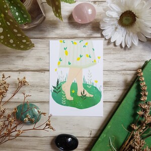 May include: A white and green illustration of a person's legs and feet walking on green grass with flowers. The person is wearing a white dress with a lemon pattern.
