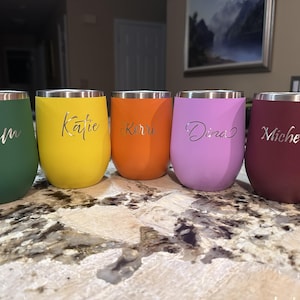 Puede incluir: Cinco vasos de vino sin pie de colores en verde, amarillo, naranja, morado y burdeos. Cada vaso tiene un borde plateado y est&aacute; personalizado con un nombre en fuente cursiva: Pam, Katie, Kirru, Dina y Michelette.