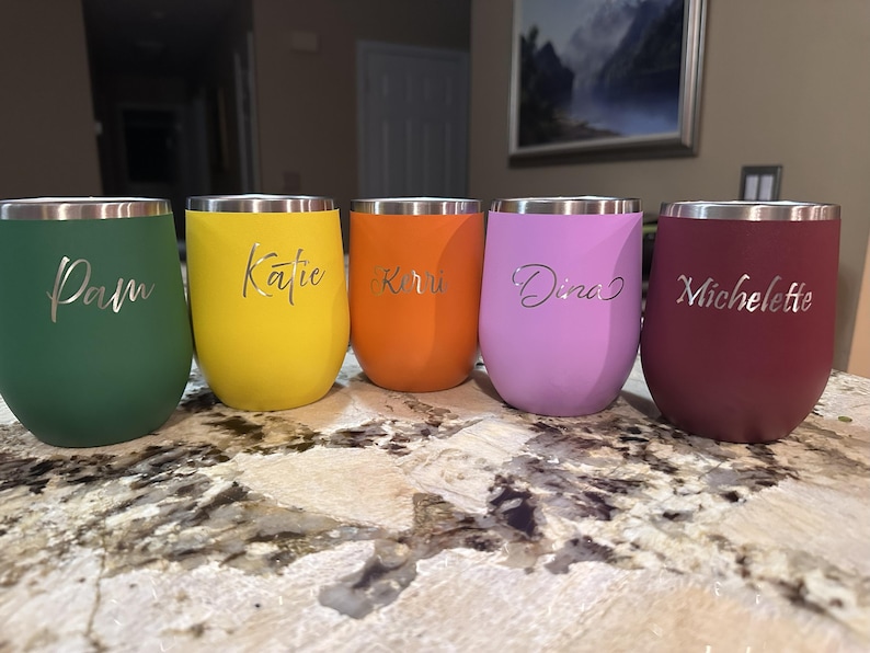 Puede incluir: Cinco vasos de vino sin pie de colores en verde, amarillo, naranja, morado y burdeos. Cada vaso tiene un borde plateado y est&aacute; personalizado con un nombre en fuente cursiva: Pam, Katie, Kirru, Dina y Michelette.