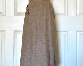May include: A knee-length, brown skirt with a subtle textured pattern. The skirt features decorative details on the waistband and a slit at the front hem. The skirt is displayed on a mannequin against a white door.